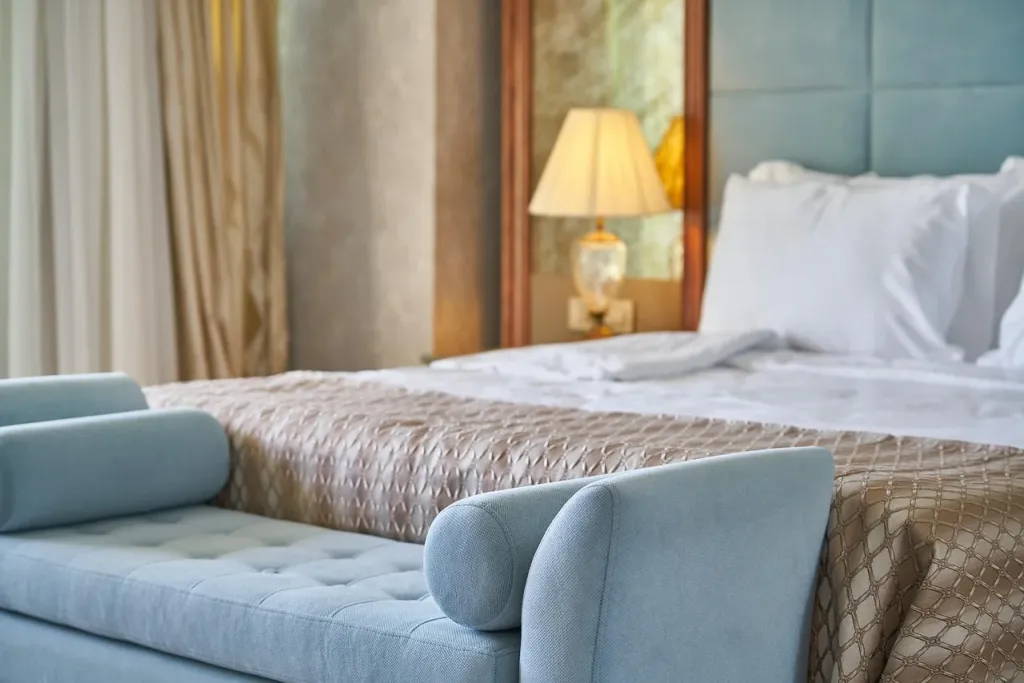 Luksusowe łóżko z tapicerowanym zagłówkiem w eleganckim wnętrzu hotelowym, zapewniające komfortowy wypoczynek.